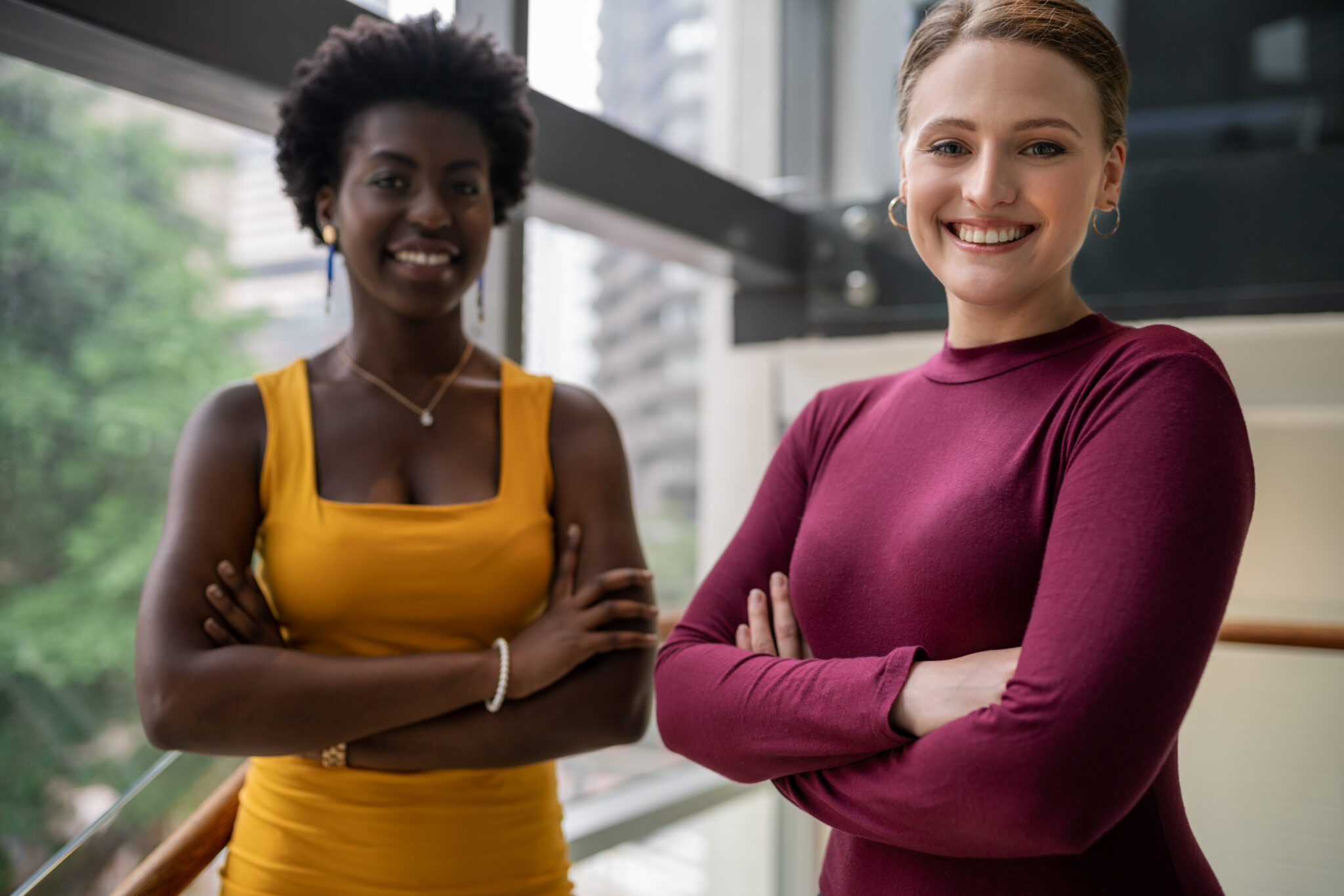 Portrait of two diverse young businesswomen smiling while standing together on some stairs in a modern office